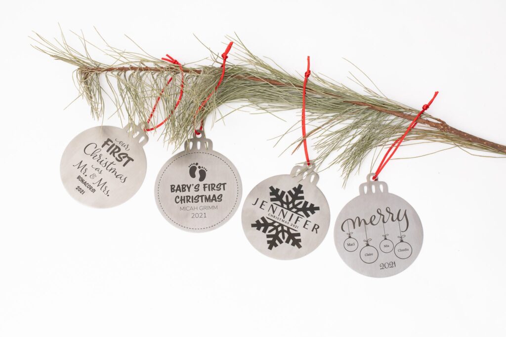 Four engraved stainless steel ornaments on a pine branch, including Baby's First Christmas and Our First Christmas as Mr. and Mrs.